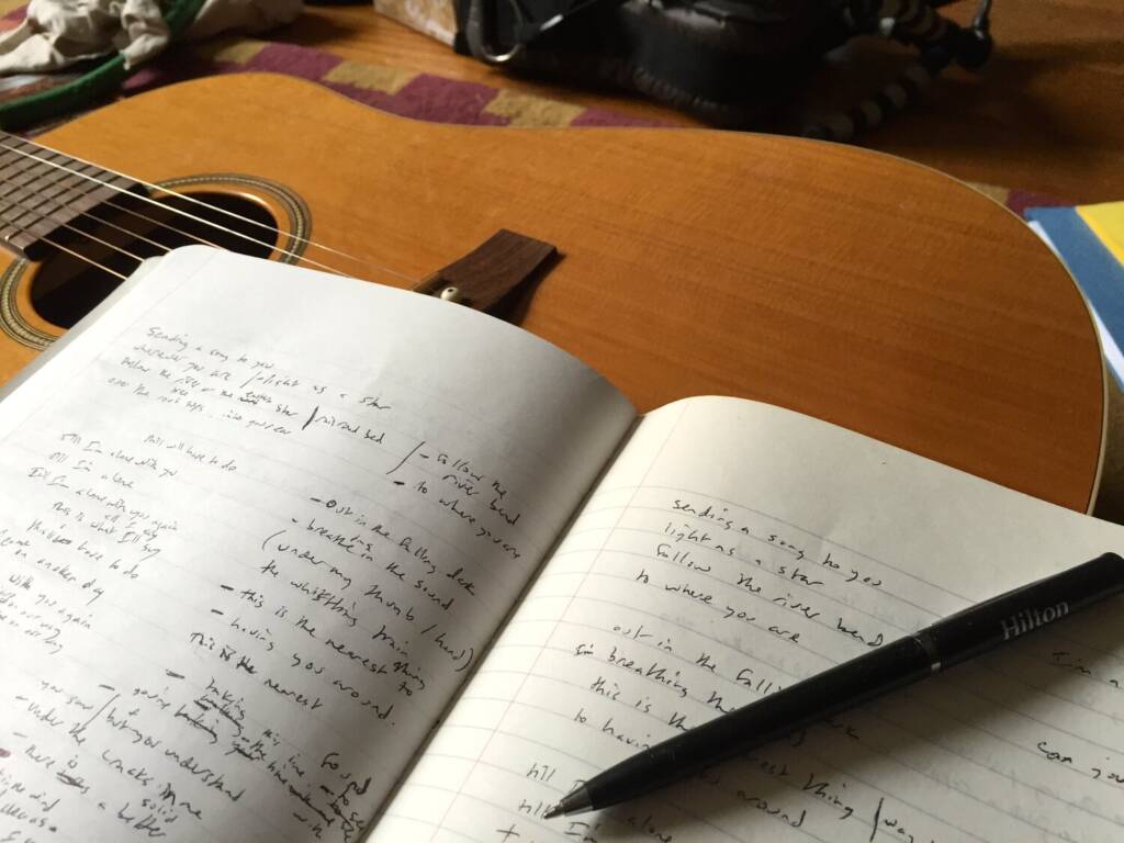 A notebook with songs written in it sitting on guitar